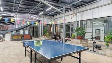 A ping pong table in a spacious indoor area with a staircase, potted plants, and exercise equipment.