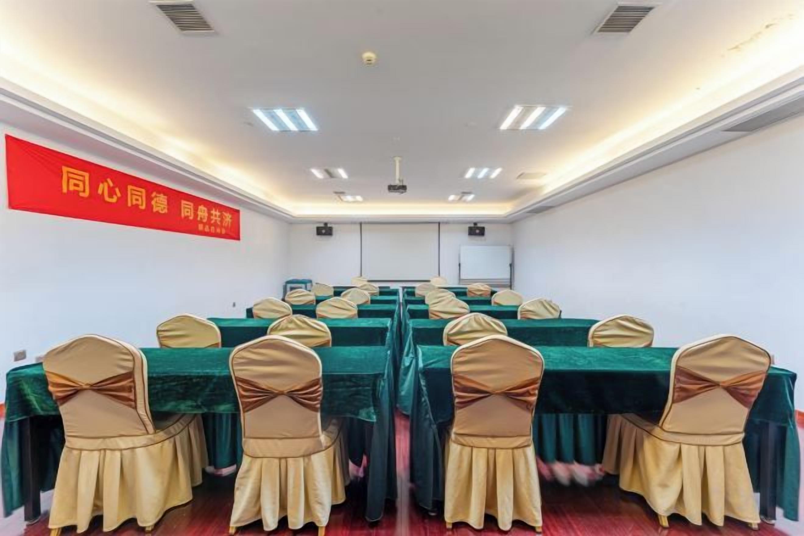 A conference room with multiple tables and chairs, a projector screen, and a red banner on the wall.