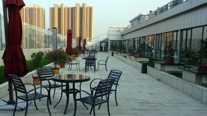 An outdoor patio area with round tables and chairs, potted plants, and red umbrellas. - Chuanyu Holiday Hotel (Dongtai)
