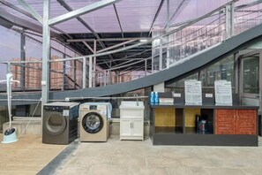 Een wasruimte met wasmachines en drogers, een trap en informatieborden.