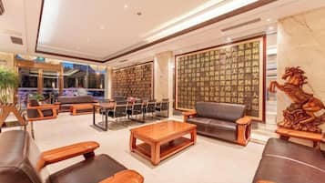 A modern hotel lobby with leather sofas, wooden coffee tables, and a decorative wall with calligraphy.