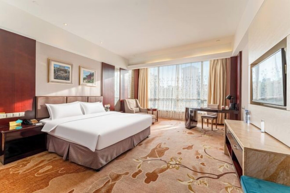 Een hotelkamer met een groot bed, een bureau, een stoel en uitzicht op het omliggende landschap.