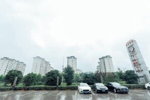 A parking lot with several cars and a tall building with red signage in the background.