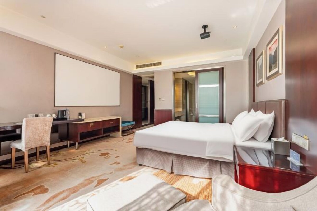Een hotelkamer met een bed, bureau, stoel en een groot raam.
