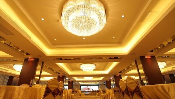 A banquet hall with rows of tables and chairs, a large chandelier, and a television screen. - Chuanyu Holiday Hotel (Dongtai)