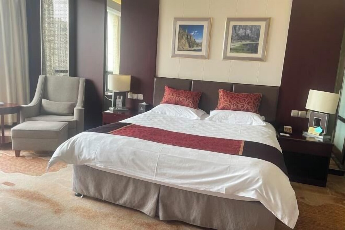 A hotel room with a large bed, two bedside tables, a chair, and two wall-mounted lamps.