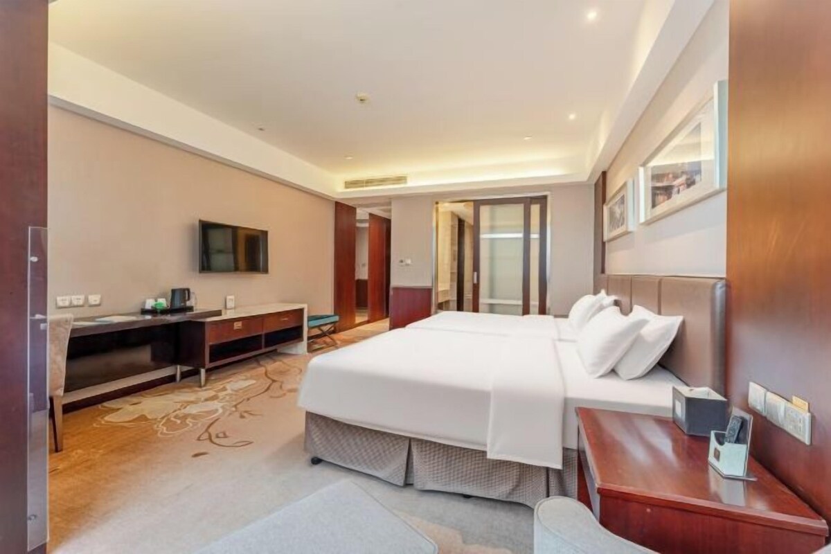 Une chambre d’hôtel avec un grand lit, un bureau, une télévision et une porte donnant sur une autre pièce.
