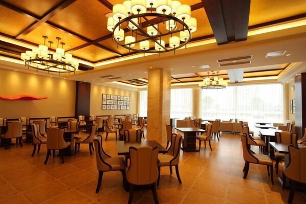 A spacious dining area with multiple tables and chairs, large chandeliers, and a modern ceiling design.