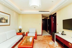 A hotel room with a sofa, armchair, coffee table, TV, and a desk with a flat-screen TV. - Chuanyu Holiday Hotel (Dongtai)