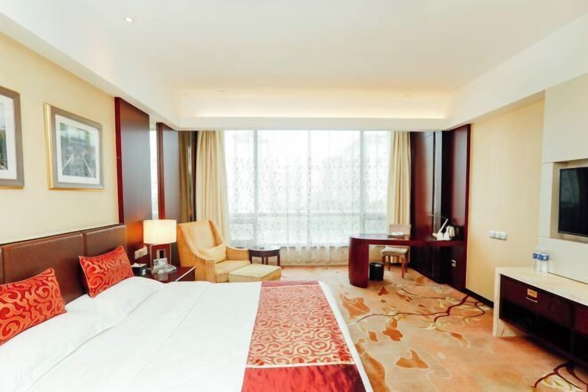 A hotel room with a bed, a desk, a chair, a TV, and a large window.