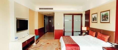 A hotel room with a bed, a TV, a desk, and a door leading to a hallway.
