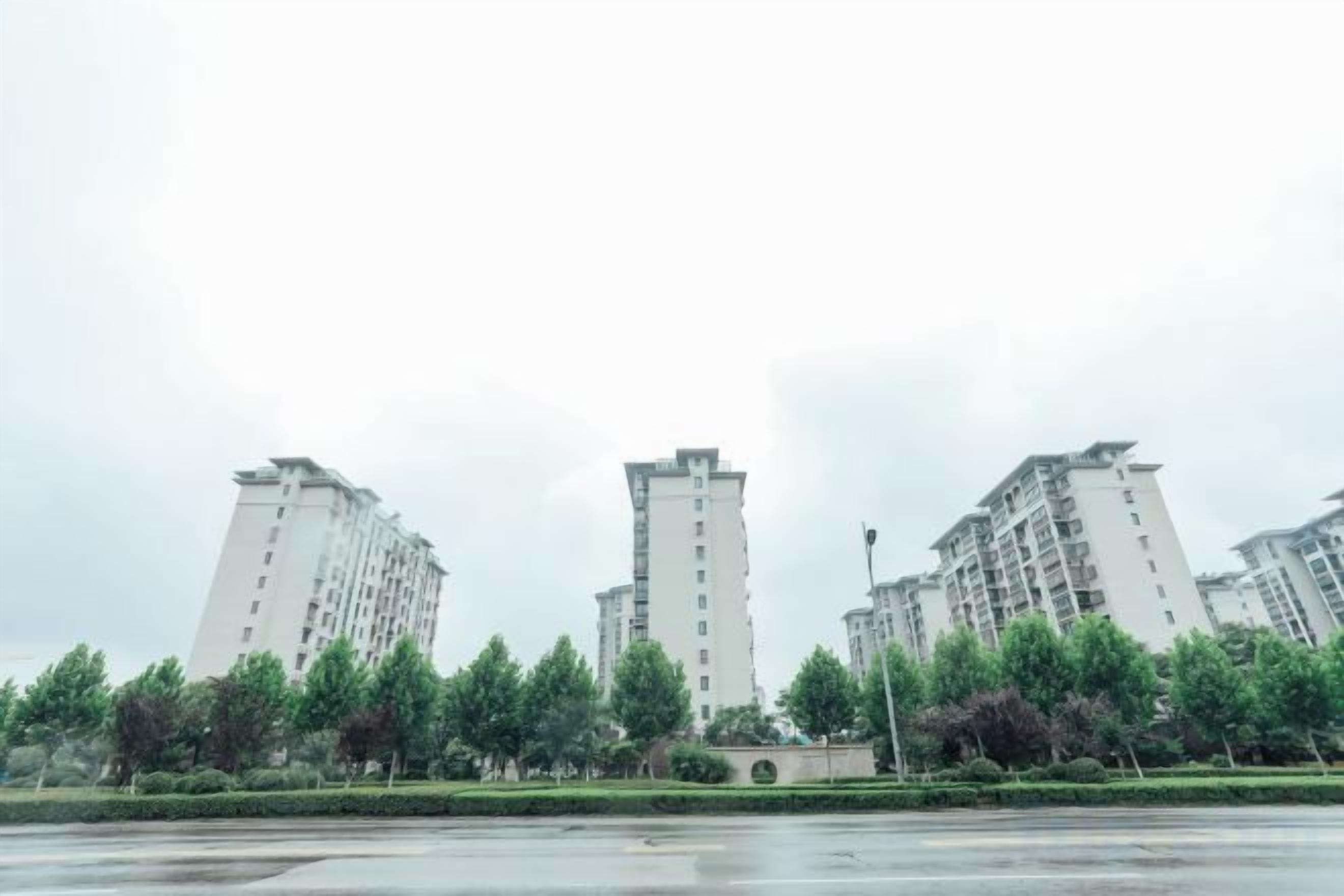 Zona residencial con edificios de gran altura, una calle pavimentada y árboles verdes.