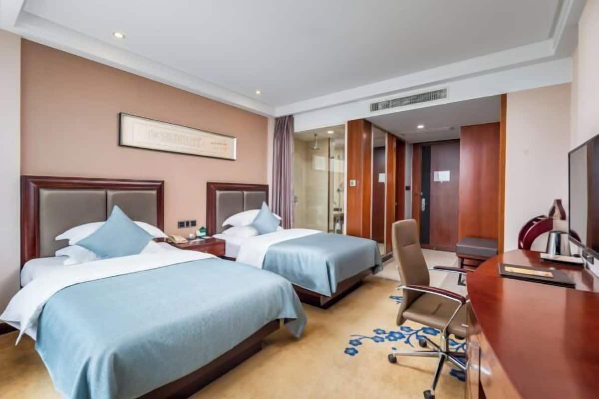 A hotel room with two beds, a desk, a chair, and a television.