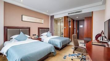 A hotel room with two beds, a desk, a chair, and a television.