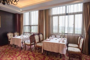 Un comedor con dos mesas dispuestas para cuatro comensales, cada una con sillas, en una habitación con ventanas amplias y una alfombra estampada.