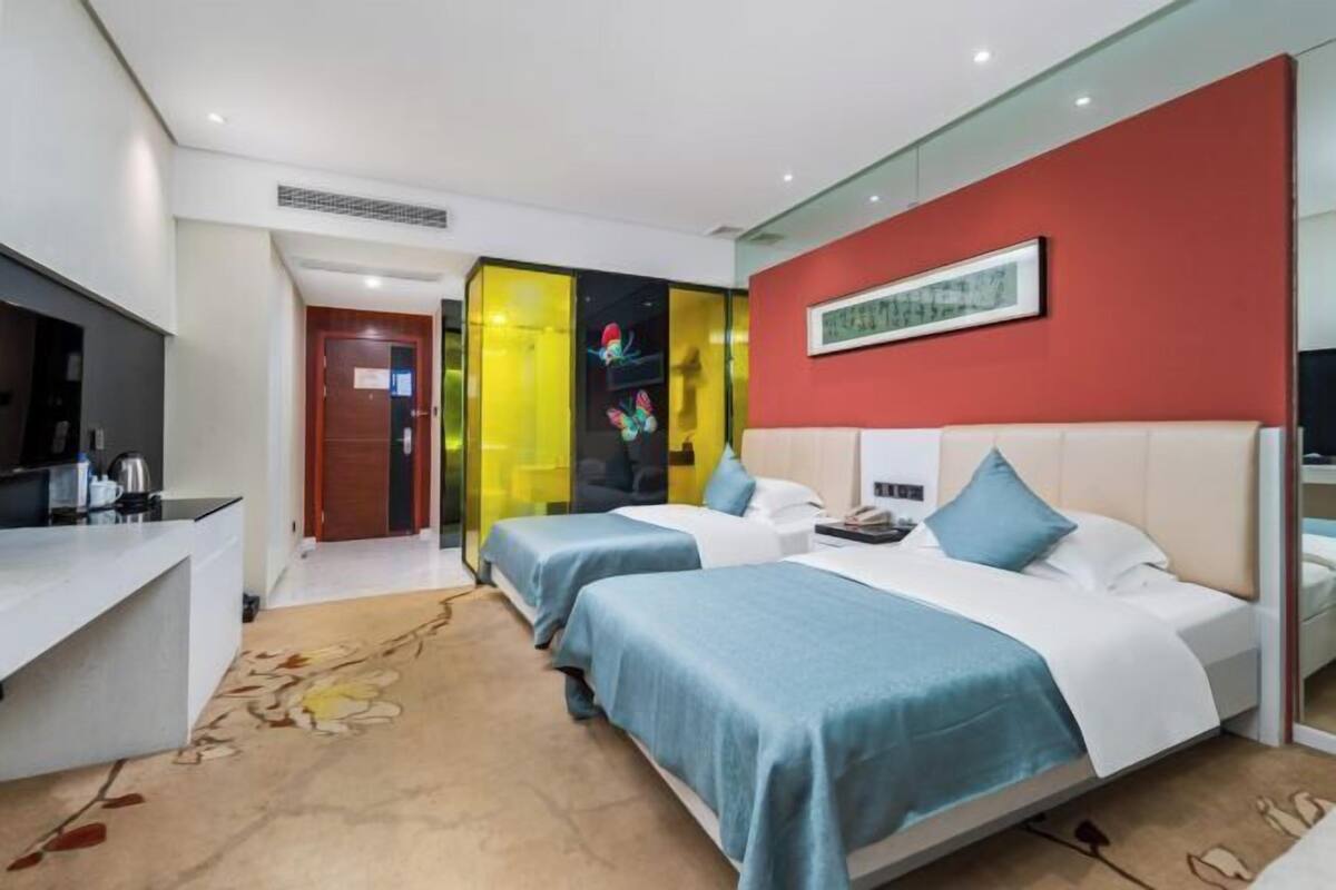 A hotel room with two beds, a desk, a mirror, and a red accent wall.