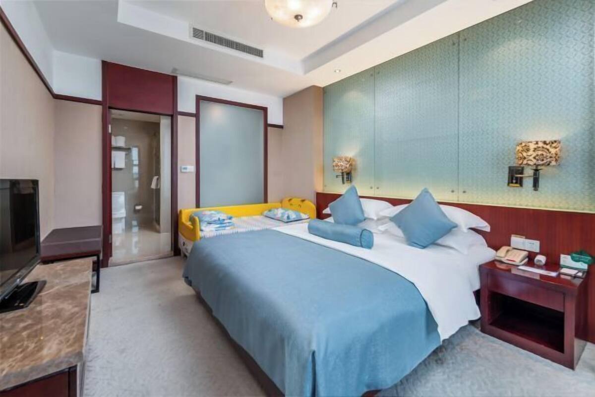 A hotel room with a bed, bedside table, TV, and a wall with a decorative panel.