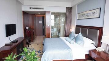 A hotel room with a bed, bedside table, TV, and a plant.