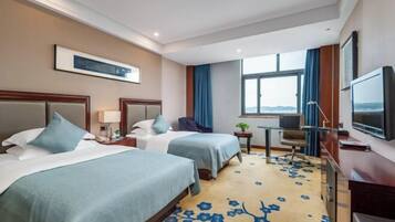 A hotel room with two beds, a desk, a chair, a TV, and a window with a view.