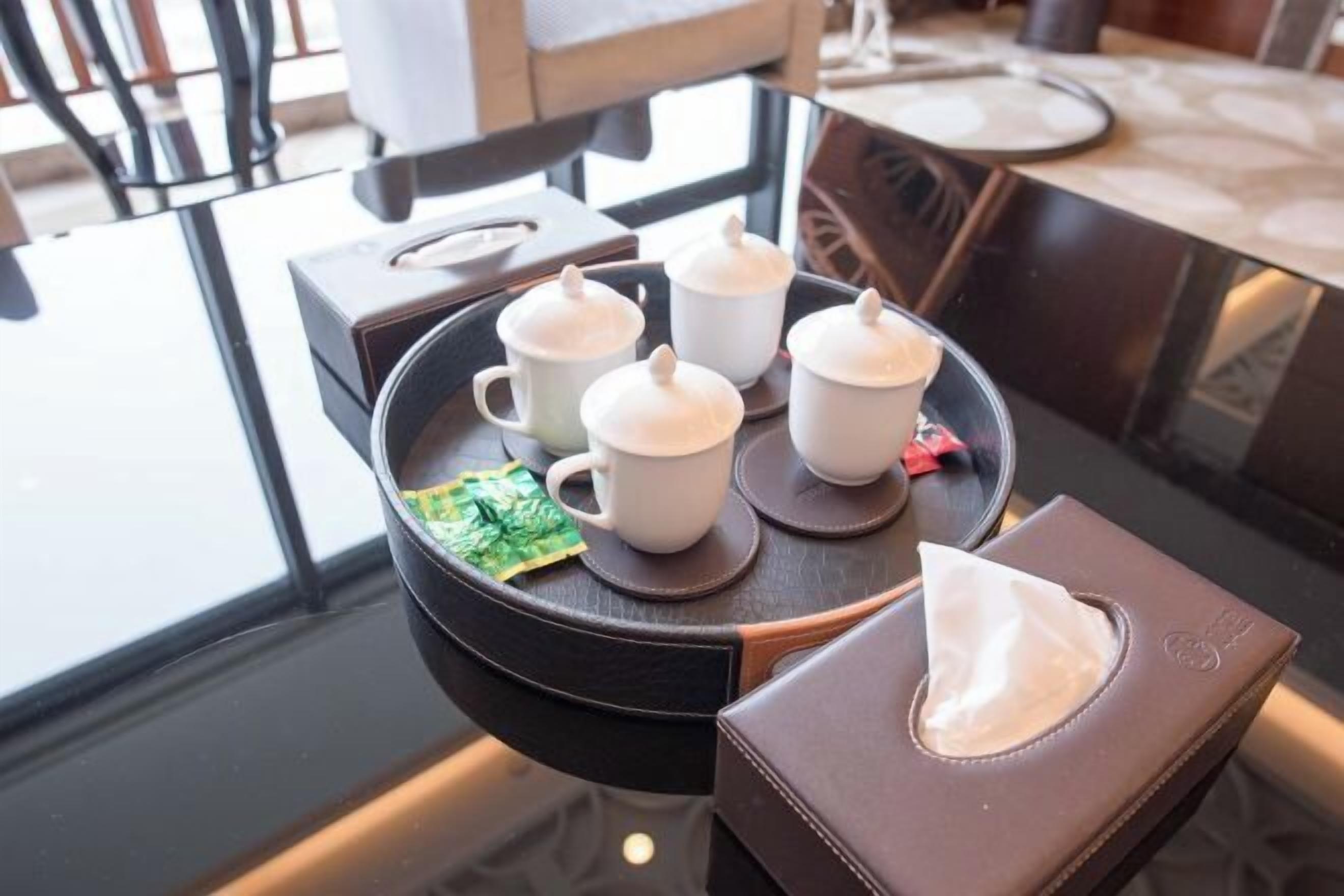 A tray with four white cups and a tissue box on a glass table.