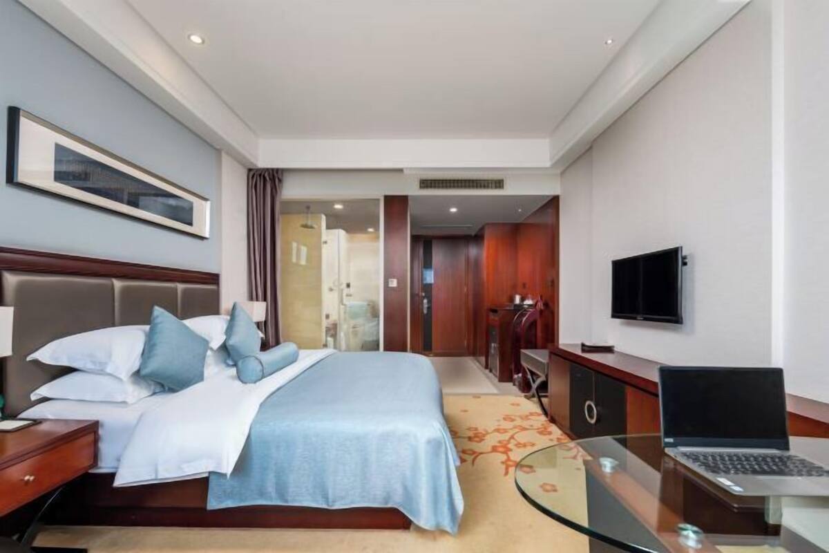 A hotel room with a bed, a desk with a laptop, a television, and a framed picture on the wall.