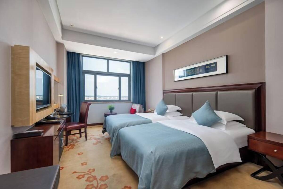 A hotel room with two beds, a desk, a TV, and a window with curtains.