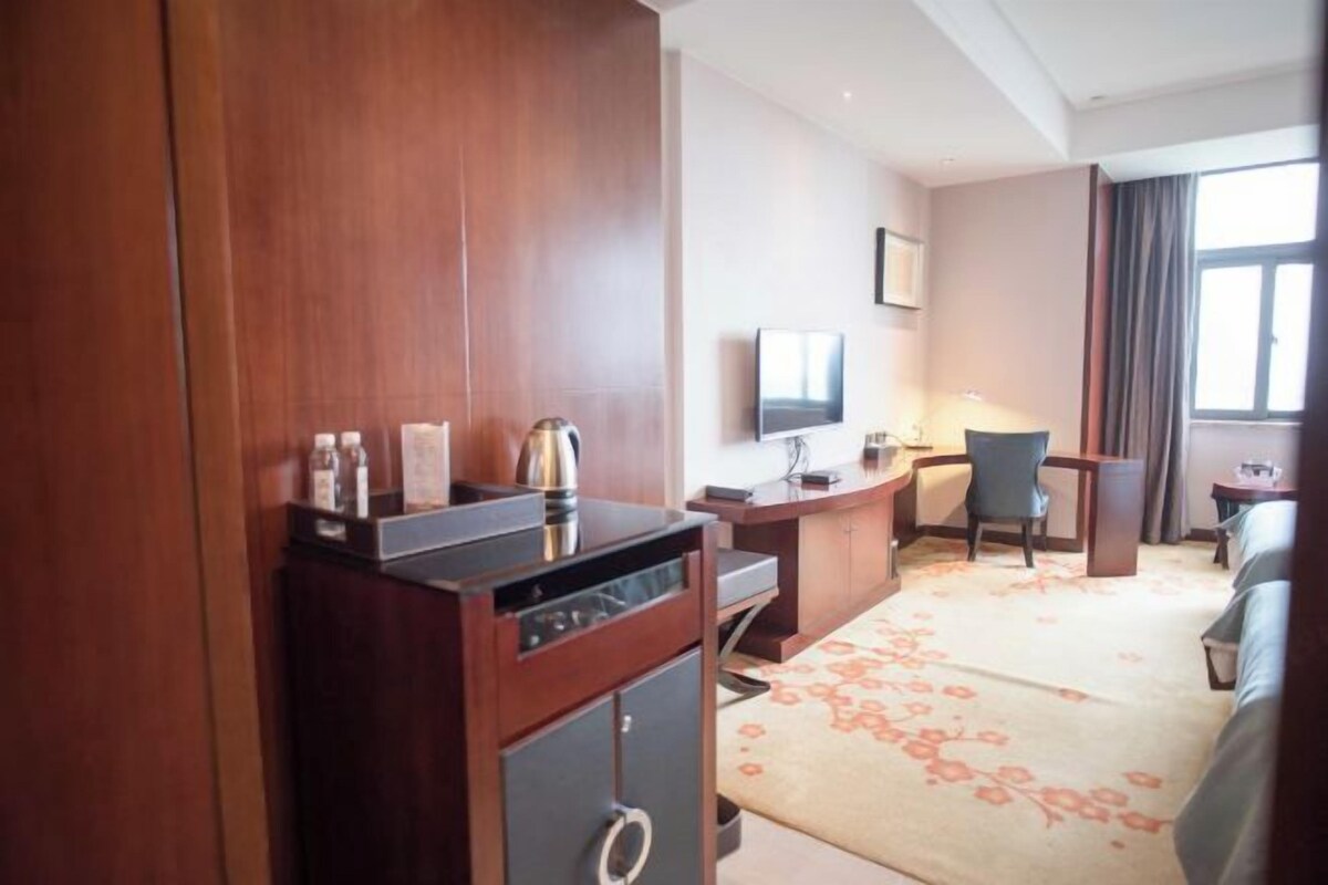 Una habitación de hotel con un armario de madera, un escritorio con una silla, un televisor y un sofá.