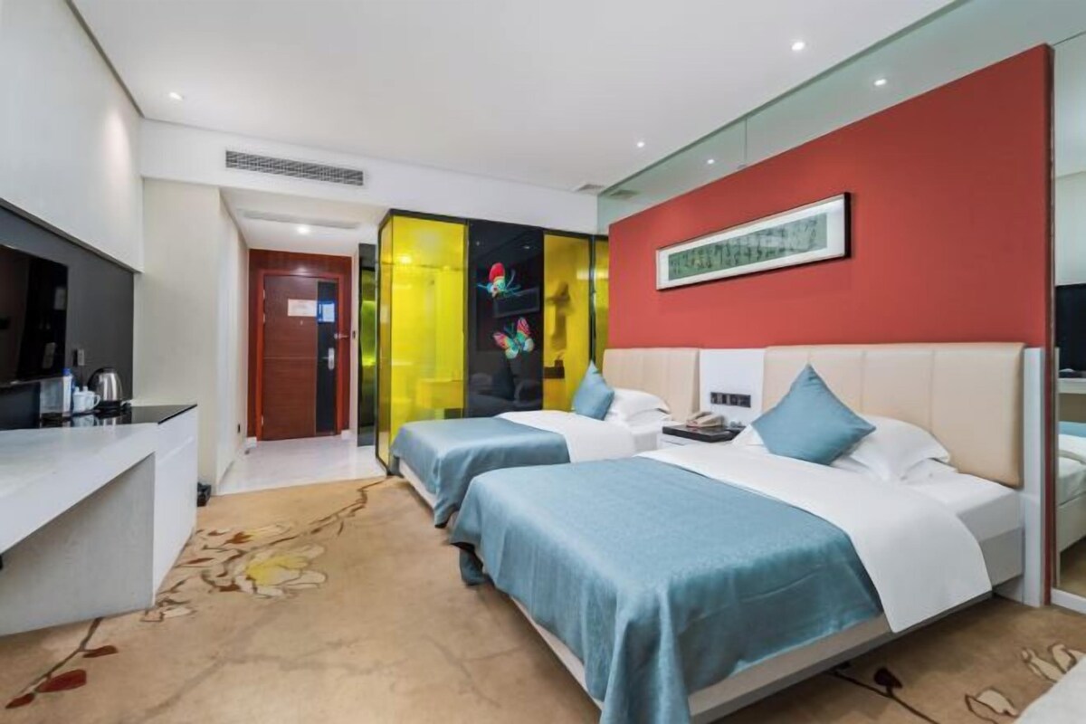 Habitación de hotel con dos camas, un escritorio, un espejo y una pared de acento roja.
