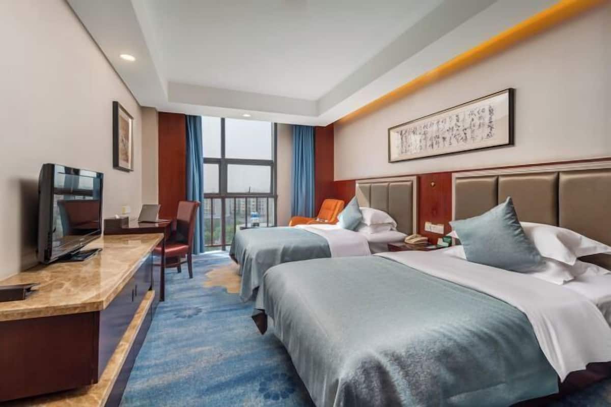 A hotel room with two beds, a desk, a TV, and a large window.