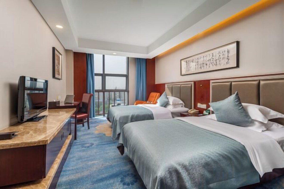 A hotel room with two beds, a desk, a television, and a large window.