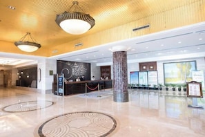 Eine großzügige Lobby mit einer Rezeption, einer hohen Holzbalkendecke und einem Marmorboden.