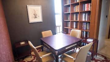 A conference room with a wooden table and four chairs, a bookshelf filled with books, and a framed picture on the wall.