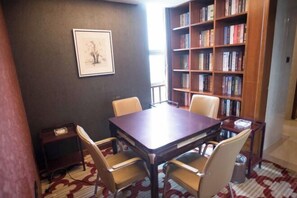 Un salón de conferencias con una mesa de madera y cuatro sillas, una estantería llena de libros y un cuadro en la pared.