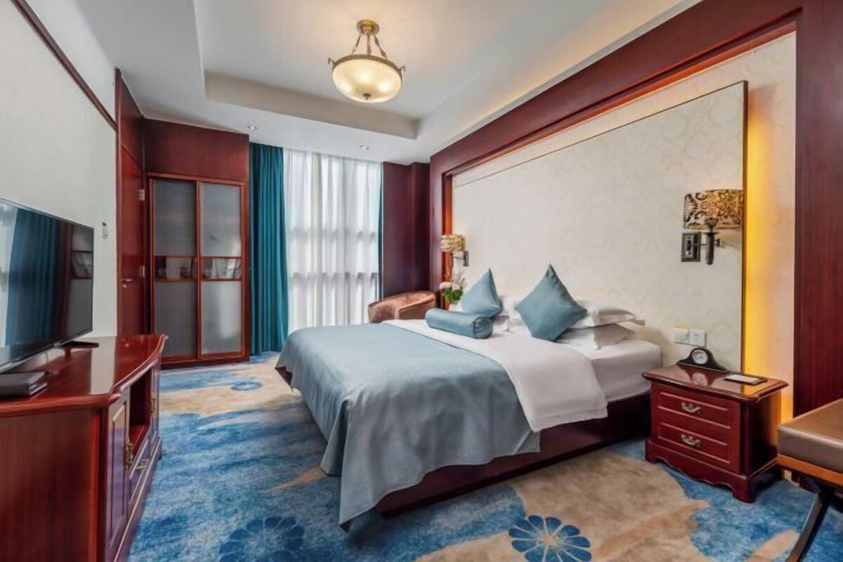 A hotel room with a bed, a TV, a desk, a chair, a wardrobe, and a large mirror.