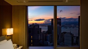 A hotel room with a large window offering a cityscape view at sunset. - One96 (Hong Kong)