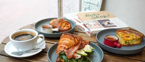 Una mesa con un croissant, una quiche, una taza de café y un menú.