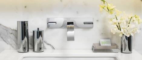 Un baño moderno con lavamanos de mármol blanco, grifería cromada y un jarrón con orquídeas blancas.