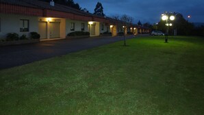 A row of motel buildings with closed garage doors, a well-maintained lawn, and a street lamp. - Motel Aeropuerto (Mos)