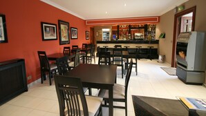 A restaurant with a red wall, multiple tables and chairs, a bar area, and a refrigerator. - Motel Aeropuerto (Mos)