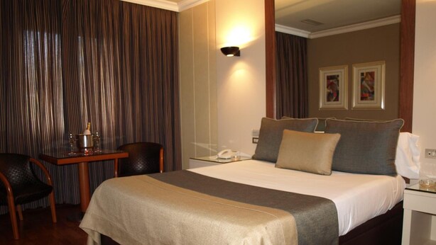 A hotel room with a bed, a desk, a chair, a nightstand, and a wall-mounted lamp. - Motel Aeropuerto (Mos)