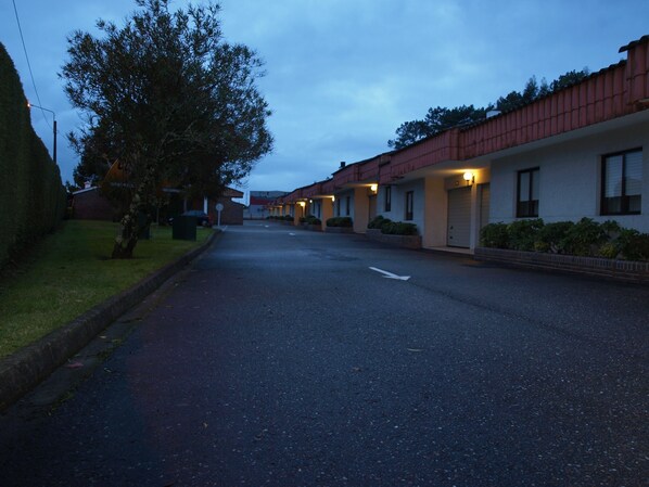 A street view of a motel with a row of single-story buildings, each with a garage door and a small front yard.