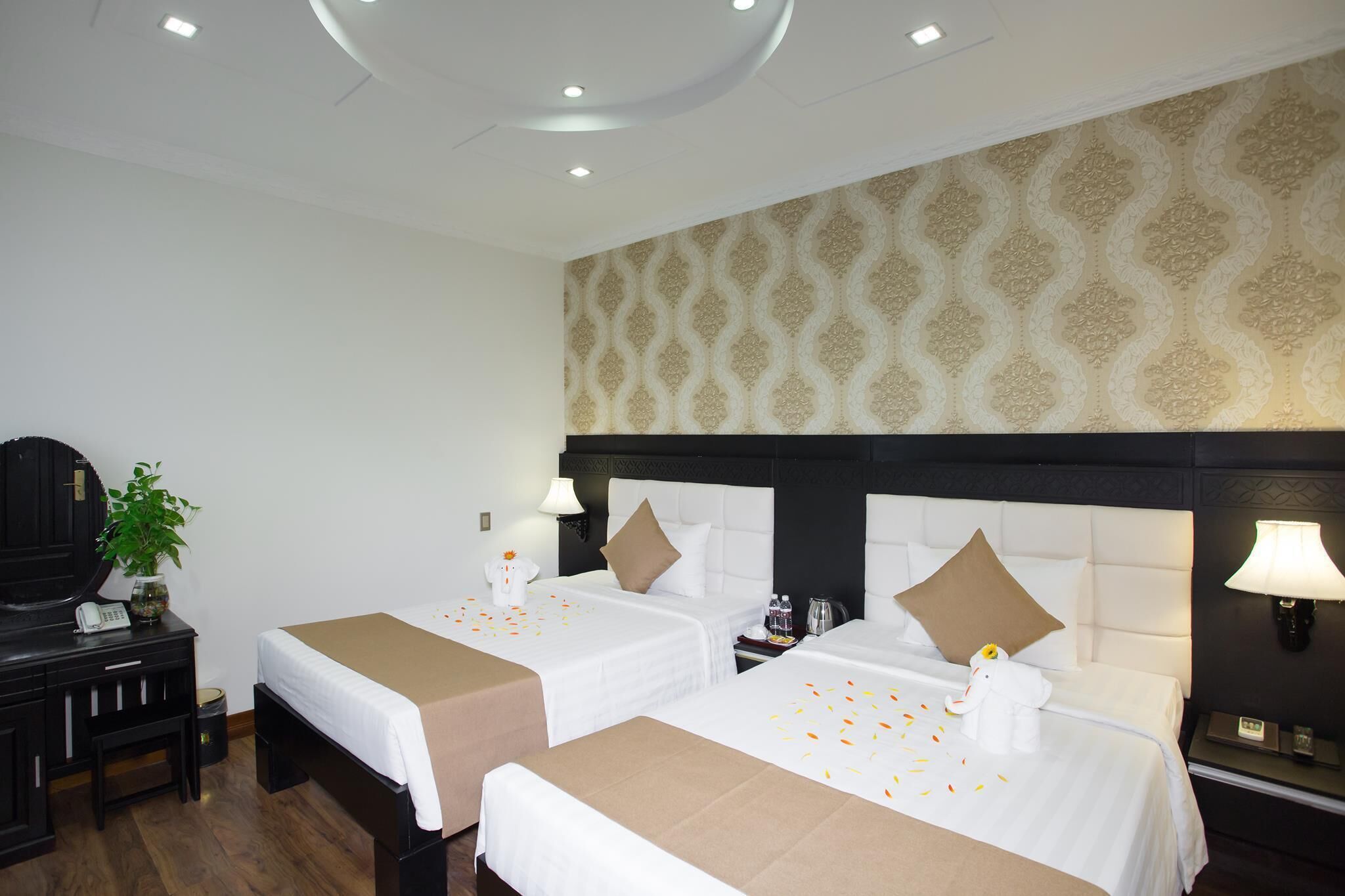A hotel room with two beds, a desk, a telephone, a lamp, and a patterned wall.