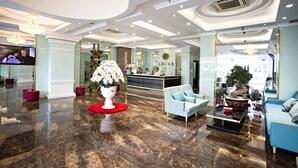 A modern lobby with a reception desk, seating area, and a large decorative plant. - Adina Hotel (Da Nang)