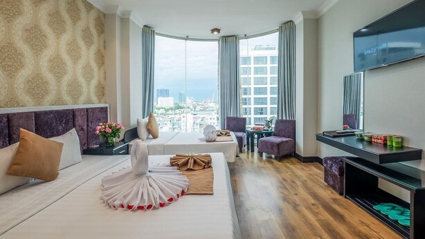 A hotel room with a large bed, a desk, a TV, and a view of the city. - Adina Hotel (Da Nang)