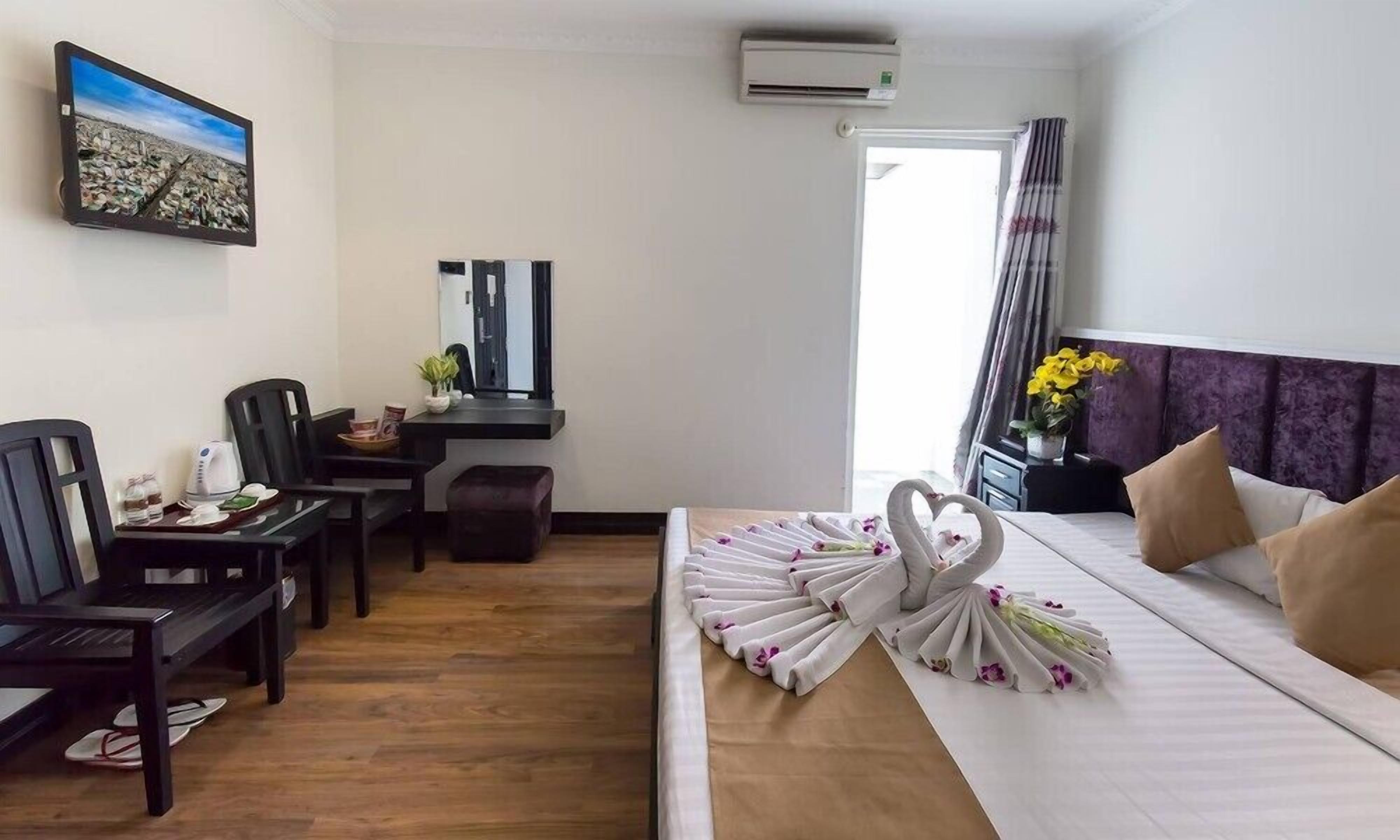 A hotel room with a bed, a desk with a chair, a small table with a plant, and a picture on the wall.