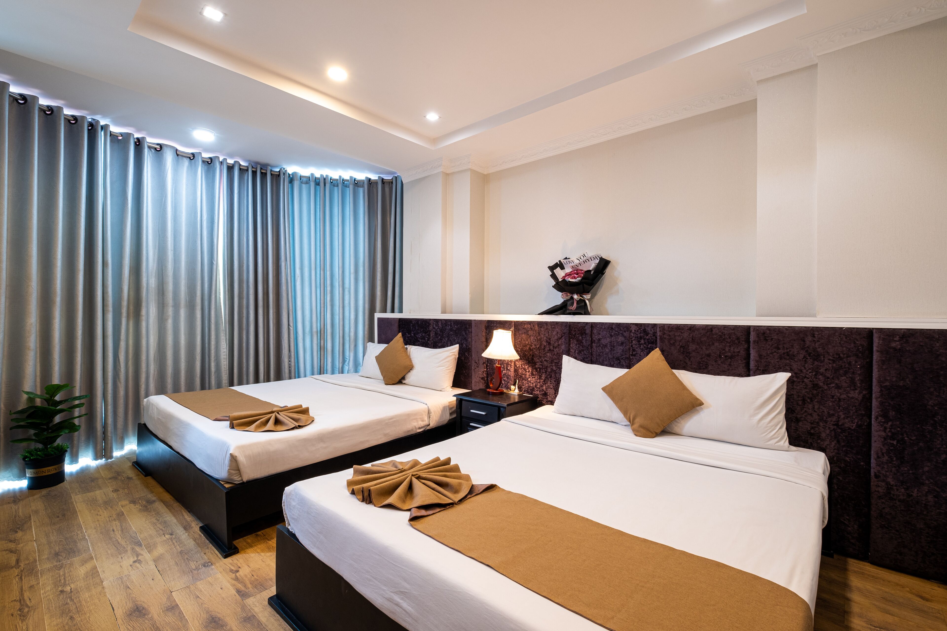 Une chambre d’hôtel avec deux lits, une table de chevet avec une lampe, une plante en pot et un objet décoratif accroché au mur.
