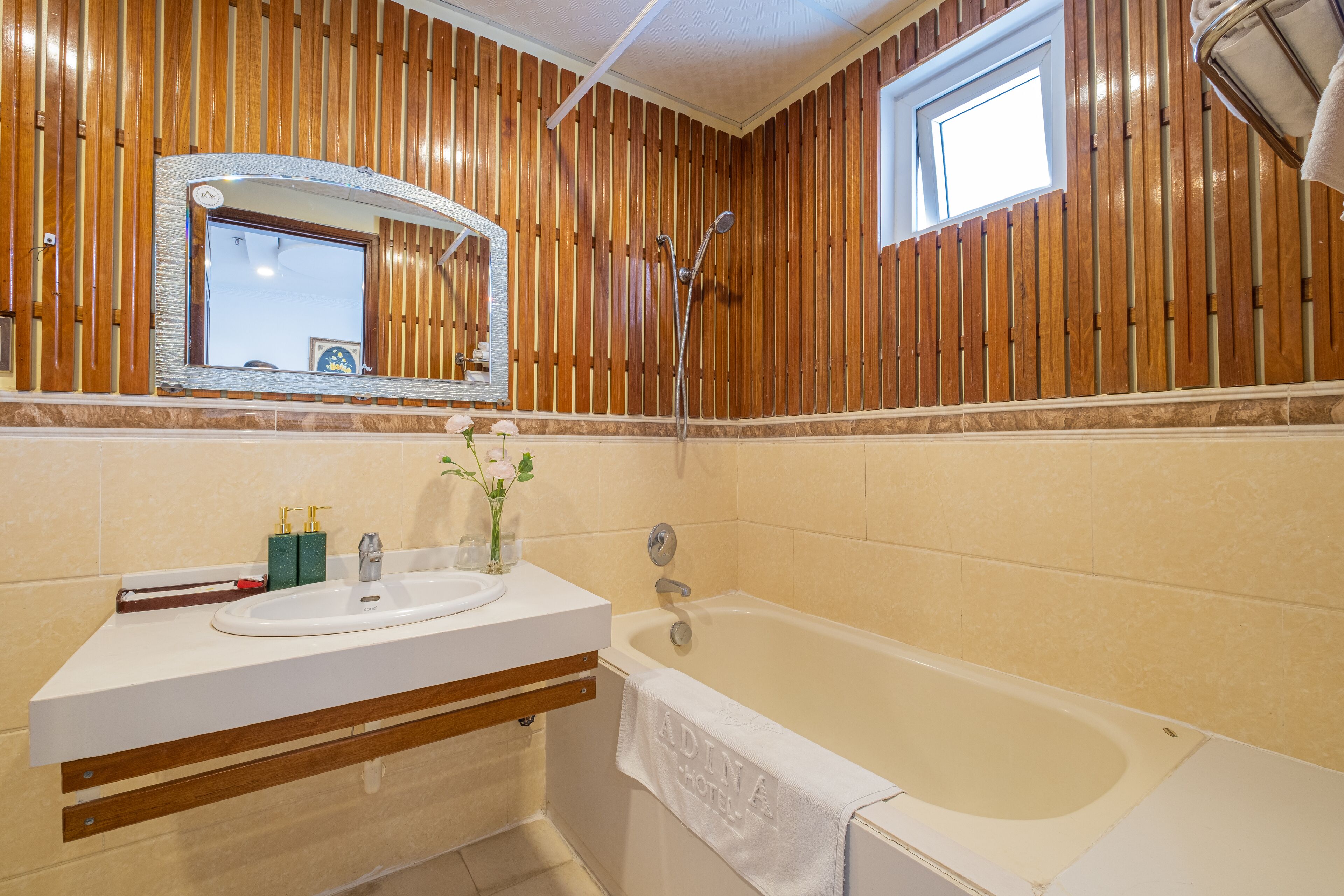 A bathroom with wooden paneling, a white sink, a bathtub, and a mirror with a picture frame.