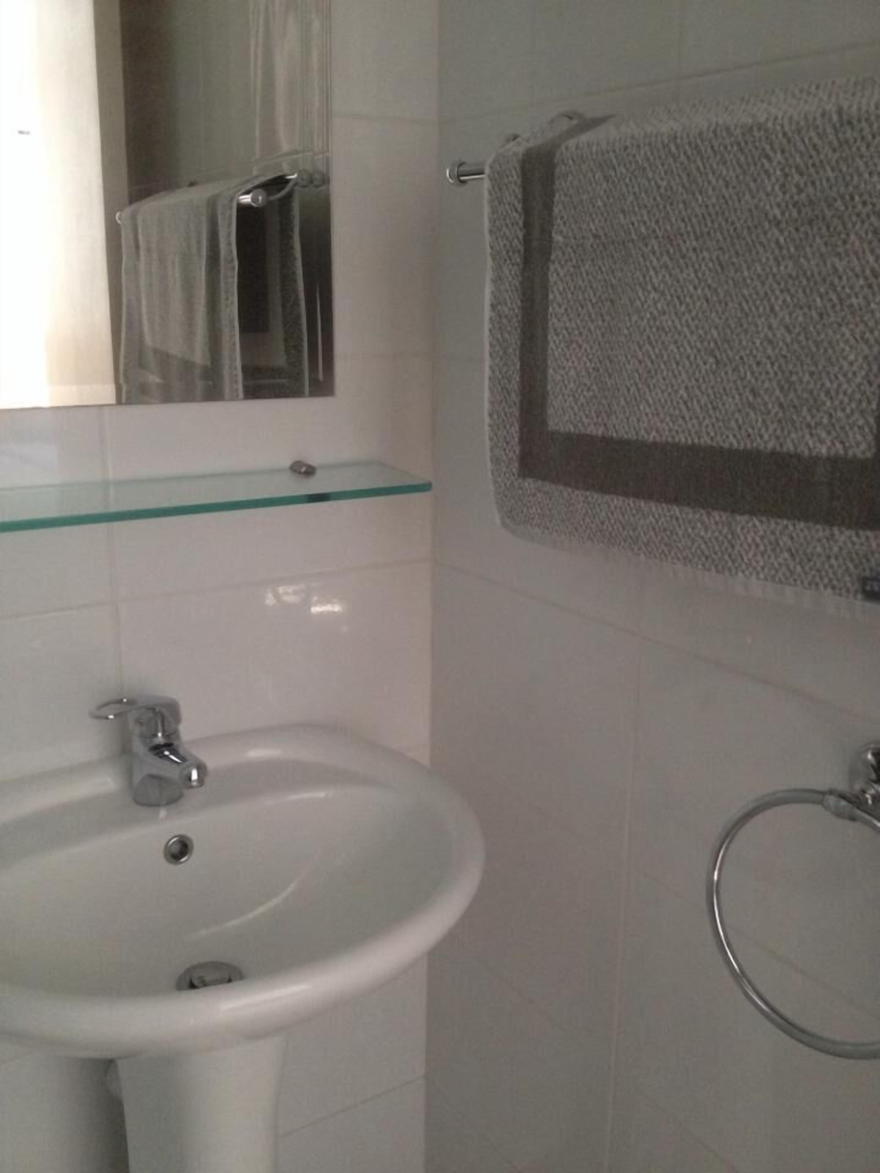 Un baño con un lavabo blanco, repisa de vidrio, toallero y espejo.