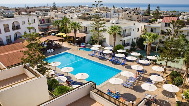 A rooftop pool area with lounge chairs and umbrellas, surrounded by buildings and palm trees. - Christabelle Hotel Apartments (Ayia Napa)
