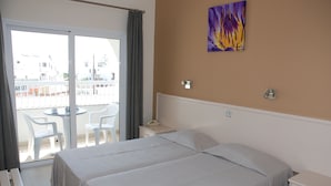 A hotel room with a bed, a bedside table, a nightstand, a window with a view of the outside, and a painting on the wall. - Christabelle Hotel Apartments (Ayia Napa)